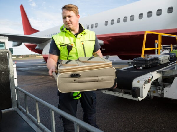 Mid adult male worker placing luggage in trailer against airplane on runway